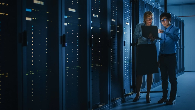 Engineer and IT Specialist Work with Server Racks, Talking, Doing System Maintenance Check with Laptop Computer