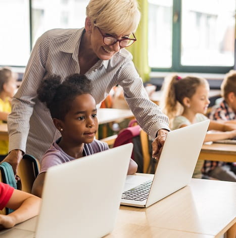 teacher helping students on laptops