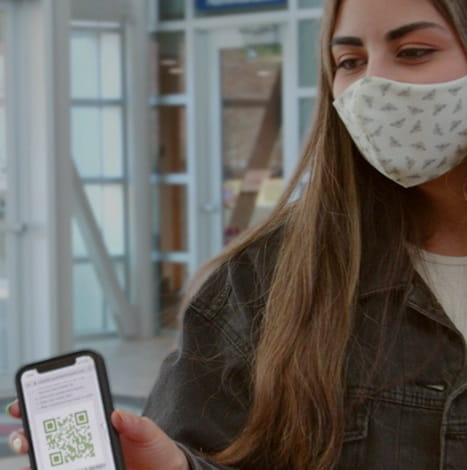 student wearing mask while holding up phone app