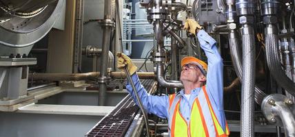 Engineer examining instrumentation cables at fuel injection stage of gas turbine which drives generators in power plant while turbine is powered down