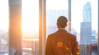 Businessman looking through office window in sunlight