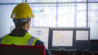 Man wearing hard hat looking at data on multiple computer screens