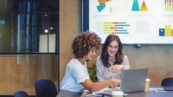 two women looking over laptop in office