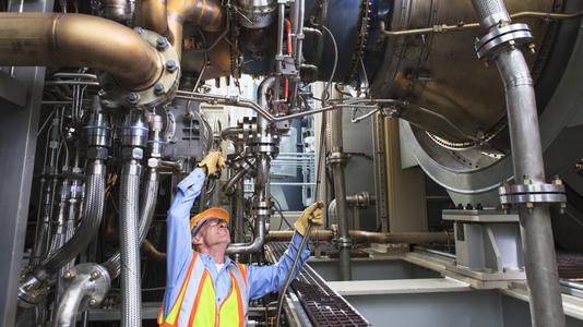 Engineer examining instrumentation cables at fuel injection stage of gas turbine which drives generators in power plant while turbine is powered down