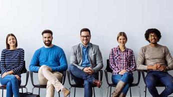 A groups of young professionals sitting in a row with their legs crossed. They are all smiling.