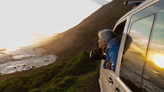 Senior woman watching sunset from her camper van