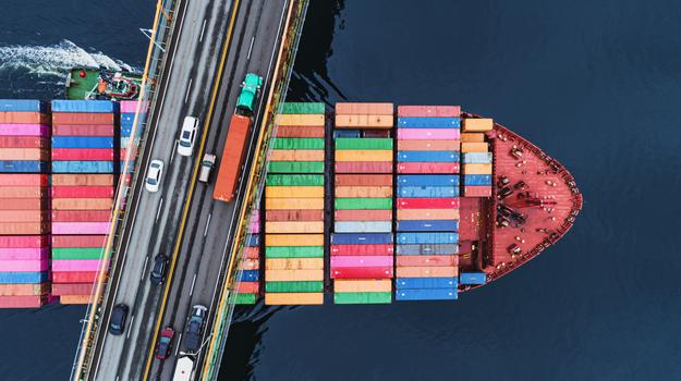 boat with shipping containers traveling under bridge